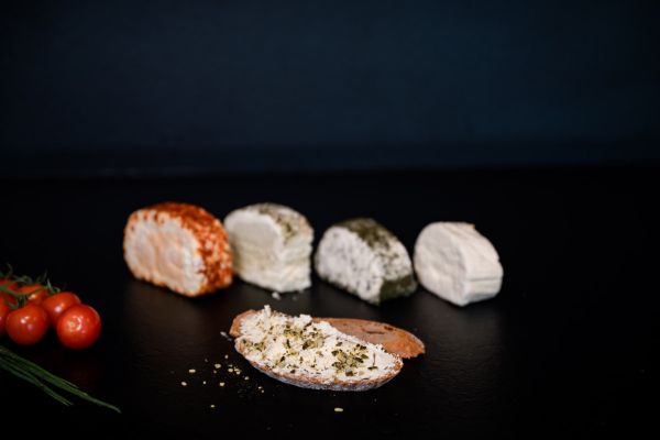 Ein Schälchen mit Frischkäse und ein Schälchen mit Kräuterquark auf einem Holzbrett auf der grünen Wiese