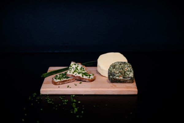 Ein rundes Stück Kräuterbutter und Butter sind auf einem Brotzeitbrett mit Brot angerichtet.