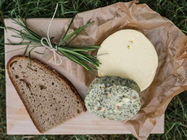 Ein rundes Stück Kräuterbutter und Butter sind auf einem Brotzeitbrett mit Brot angerichtet.