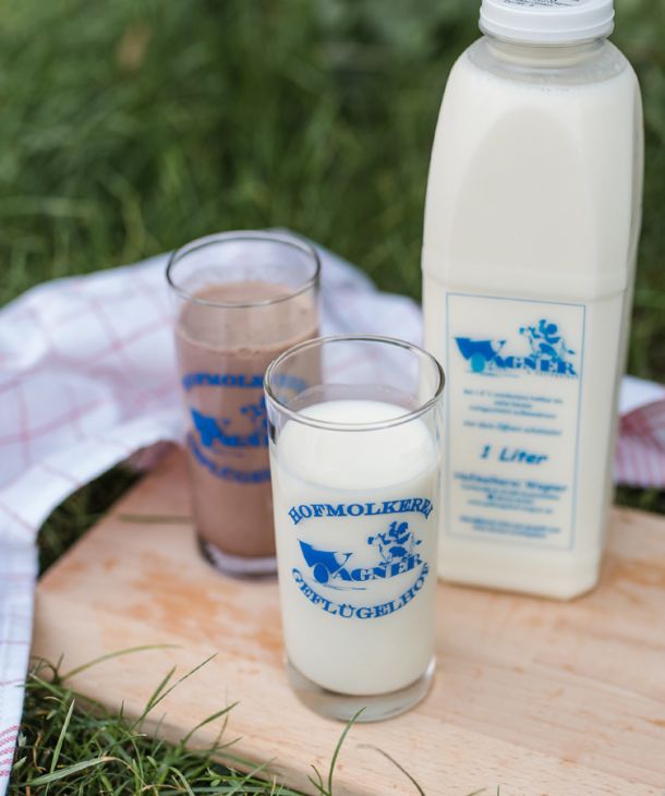 Ein Glas frischer Kuhmilch, ein Glas mit Kaba und eine Flasche Kuhmilch sind auf einem Holzbrett auf einer grünen Wiese angerichtet